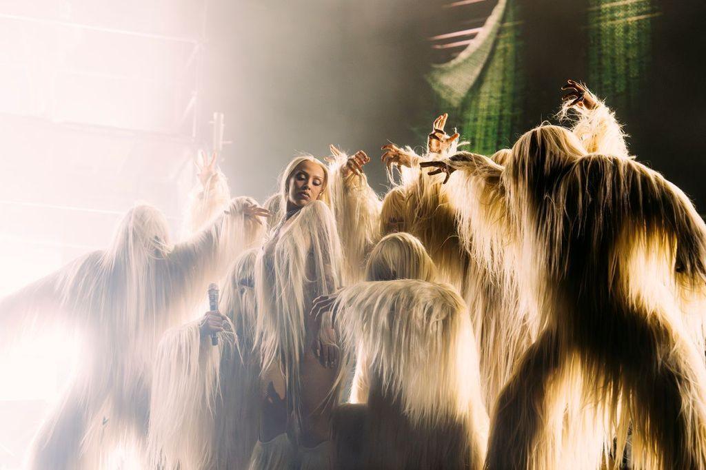 Doja Cat performing on stage with her dancers in eye-catching furry costumes.