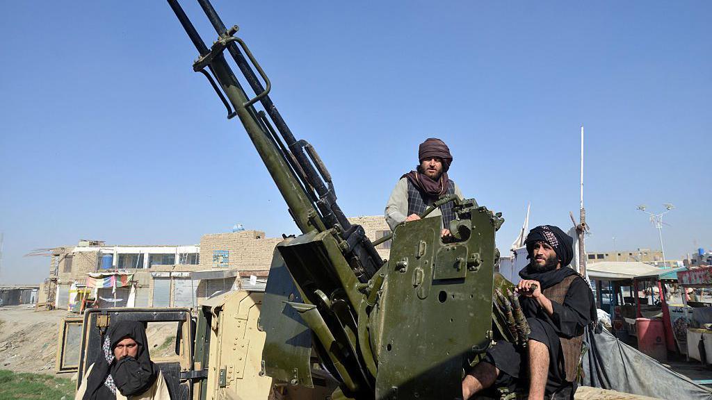 Men wearing dark coloured clothes and turbans on their heads sitting around a green missile launcher