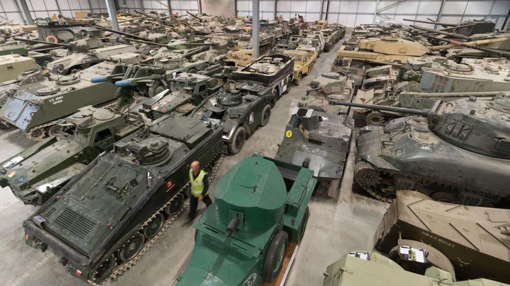 Rows and rows of tanks parked inside what looks like a large aircraft hangar.