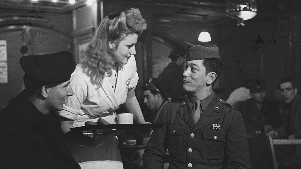 A black and white photo of an English volunteer waitress waiting on club members at Rainbow Corner, the American Serviceman's Club off Piccadilly Circus. 