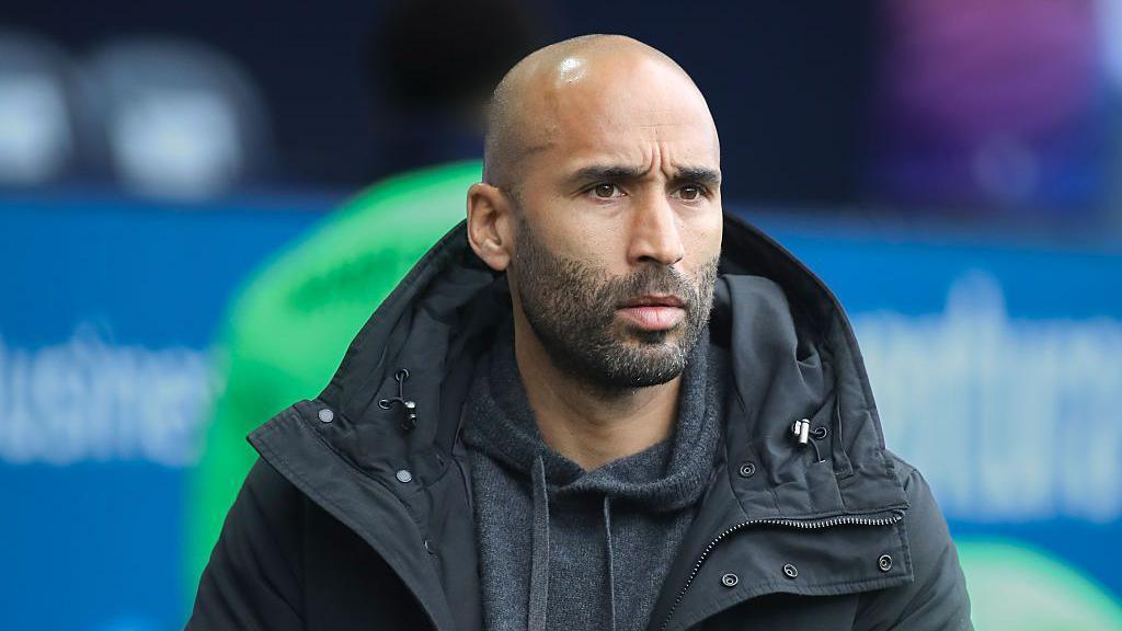 Lee Grant is on the touchline watching on during a match. He is wearing a dark grey coat