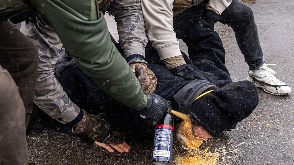 three agents pin someone to the ground and spray chemical irritant directly into their face
