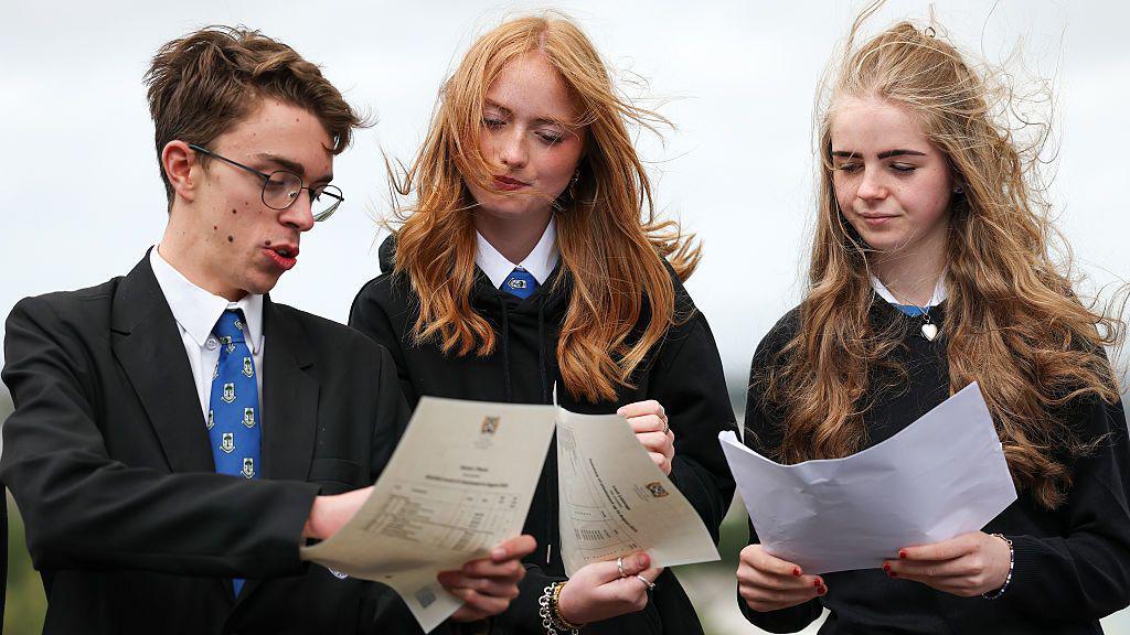 a boy and two girls in school uniform look at their exam certificates