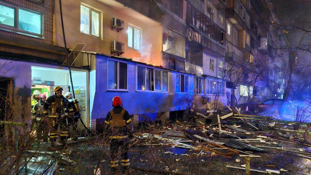 Rescue workers at the site of a Russian strike in Kyiv, standing amongst the rubble in front of a building