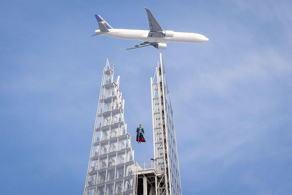 A plane flies over the Shard with a model of Superman - with his red cape and blue suit - suspended above the viewing platform. 