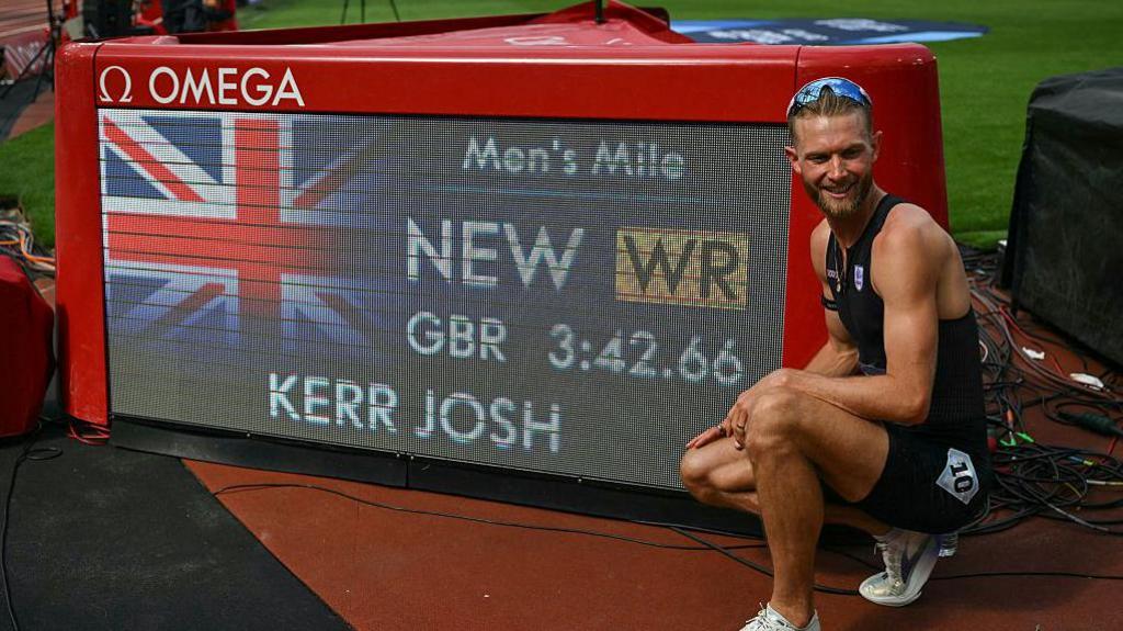 Josh Kerr poses next to a screen displaying his world record time