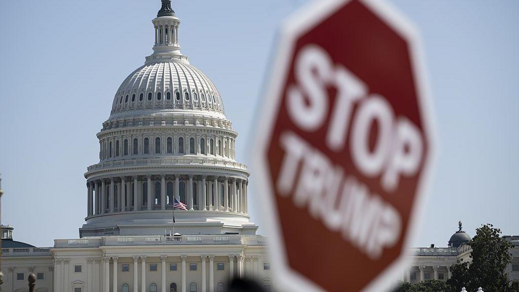 File image of the US Capitol building with a blurry sign in the foreground that reads "Stop Trump"