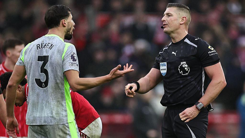 Match referee Robert Jones talks to Ruben Dias of Manchester City