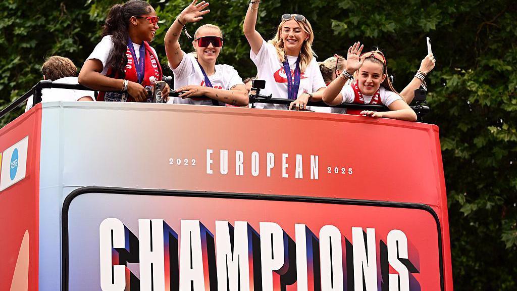 Georgia Stanway, Chloe Kelly and Ella Toone of England seen waving from top deck of bus, which has the text 2022, 2025 European Champions