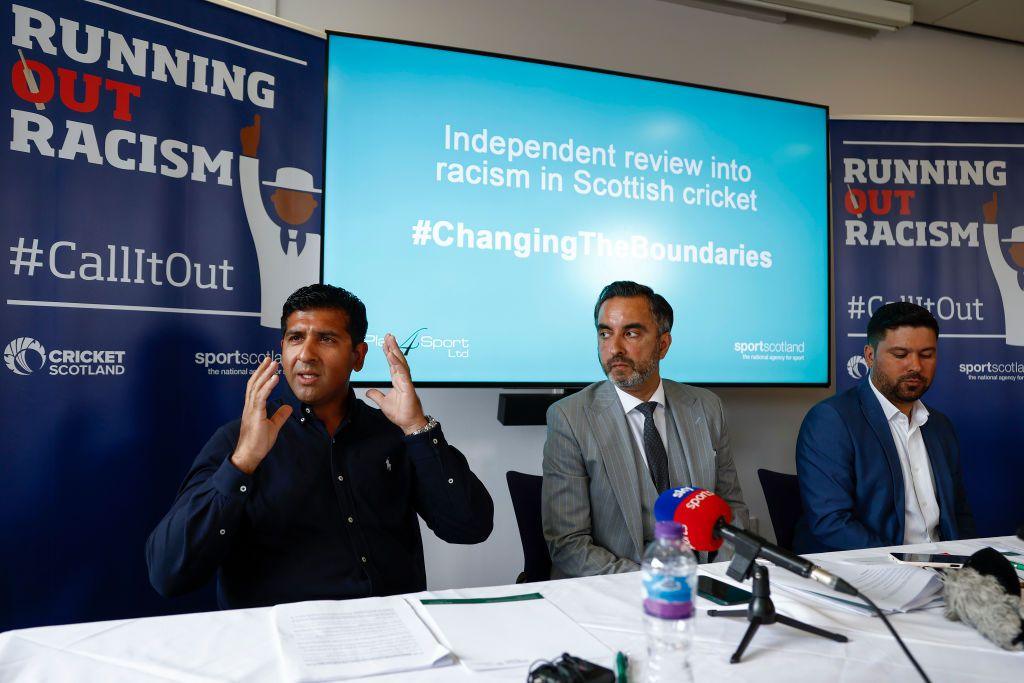 Majid Haq and Qasim Sheikh hold a news conference with lawyer Aamer Anwar at the Stirling Court hotel on July 25, 2022 in Stirling. They are dressed casually in dark blue and white open necked shirts and Mr Anwar is in the middle in a grey three-piece suit. There is a mic on the table and Running Out Racism branded boards behind them.