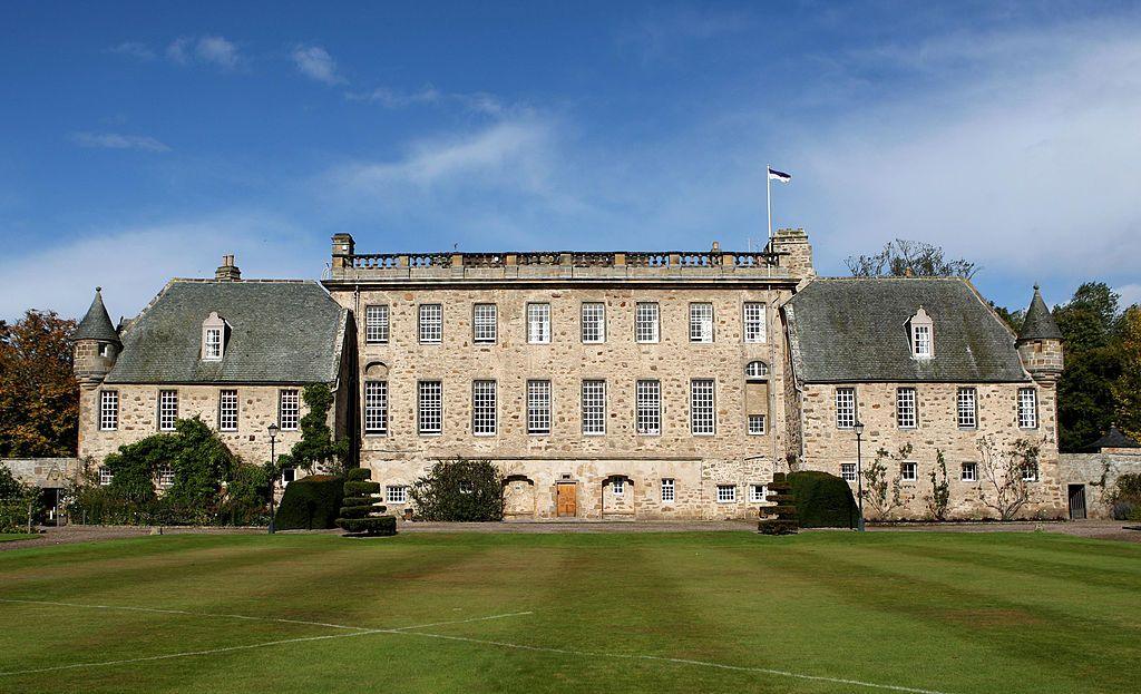 An old three-storey school building with turrets with a grass lawn