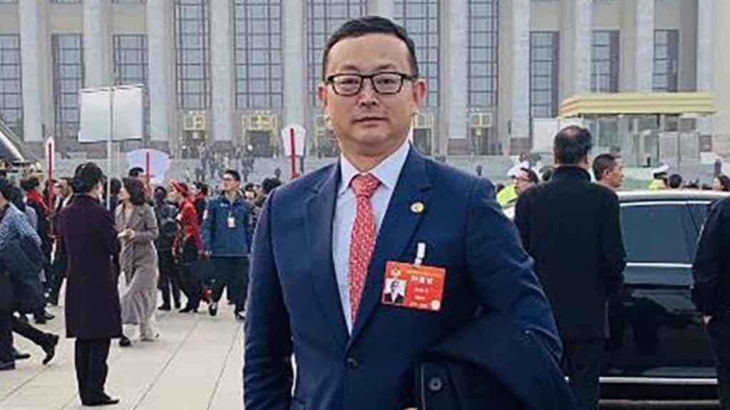 Yang Tengbo wearing a suit and glasses in front of a government building in Beijing
