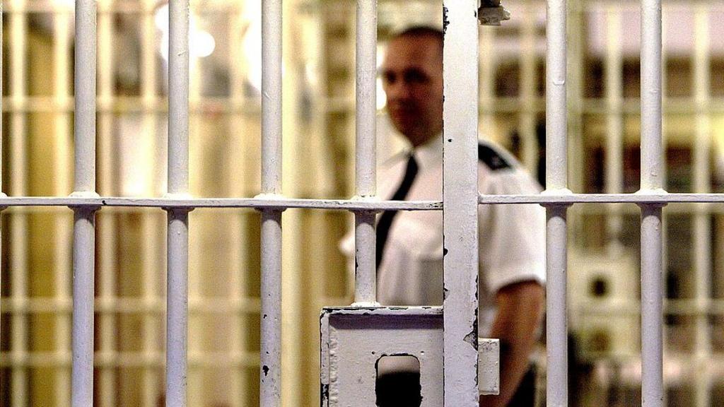 A prison guard at HMP Pentonville stands behind a locked gate (file photo)