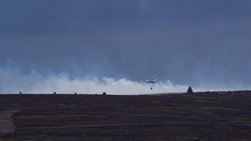 A helicopter drops water onto the flames