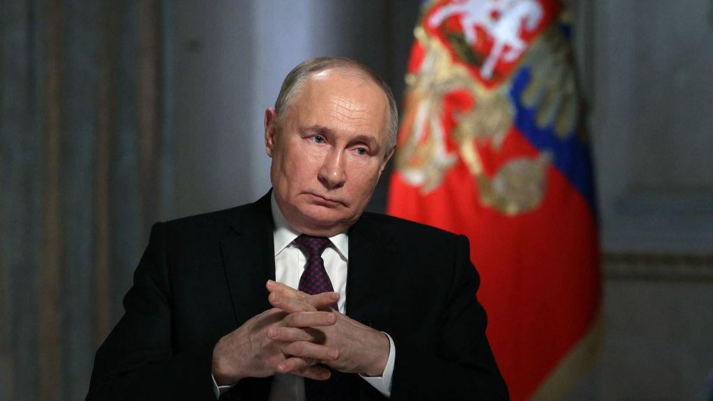 Vladimir Putin staring with his hands crossed. 