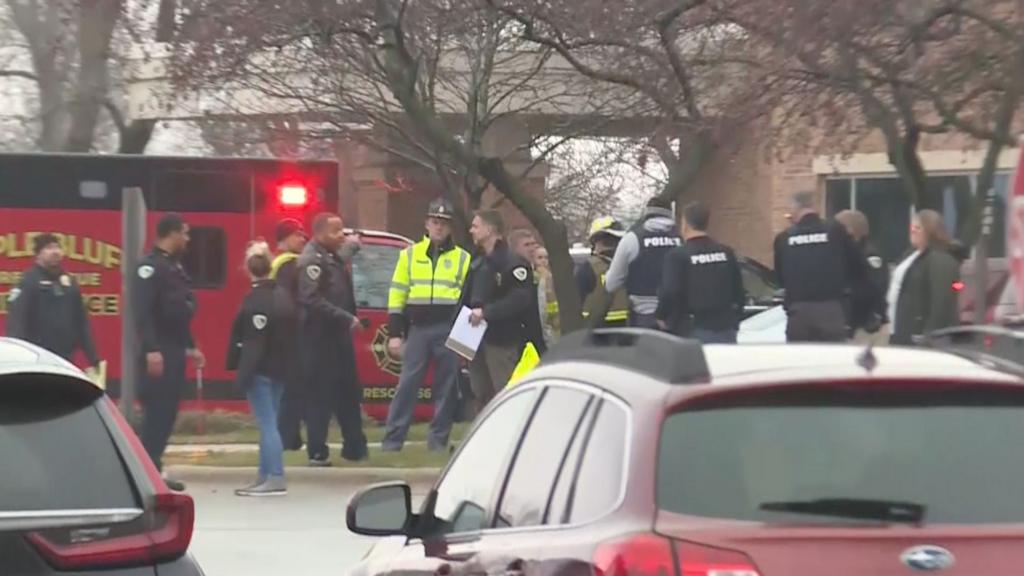 Police and emergency responders stand in front of flashing lights in a school car park