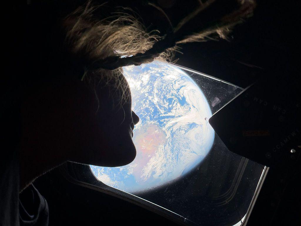 astronaut and Artemis II mission specialist Christina Koch peers out of one of the Orion spacecraft's main cabin windows, looking back at Earth.