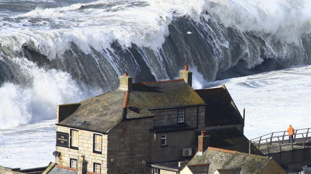 A large wave crashes over the beach at Chiswell in 2014. In the foreground are seafront buildings including a pub.