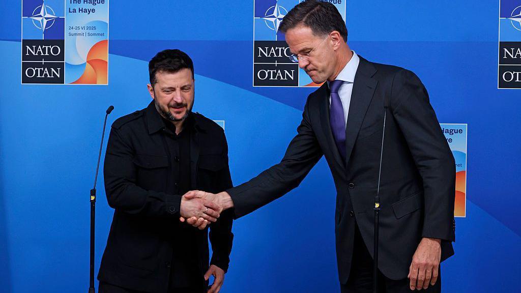 The Ukrainian leader on the left wearing black shakes hands with the taller Dutch Nato Secretary General Mark Rutte against a blue background