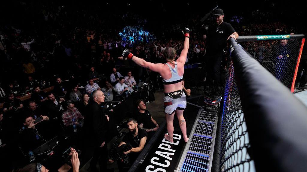 Molly McCann celebrates on the side of the cage with fans