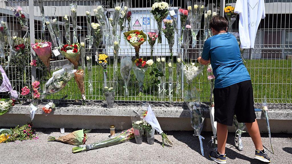 A boy hangs flowers on the fence of his school