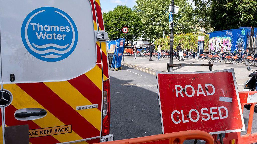 The back of a Thames Water van with the blue logo on the door, with a "road closed" sign next to it.
