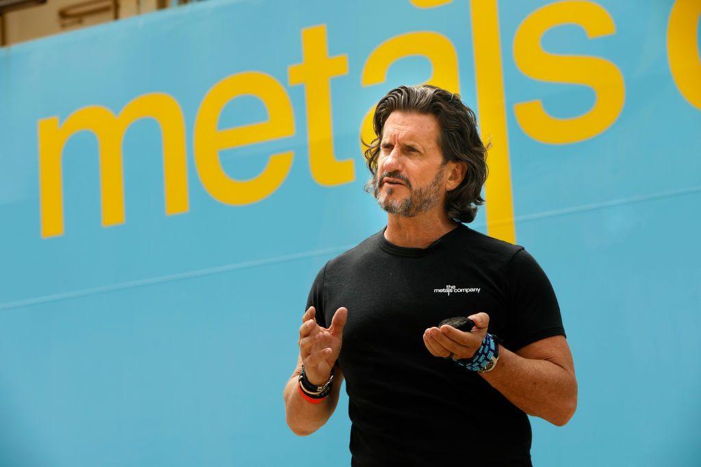 Wearing a black t-shirt and multiple bracelets Gerard Barron stands beside a ship.