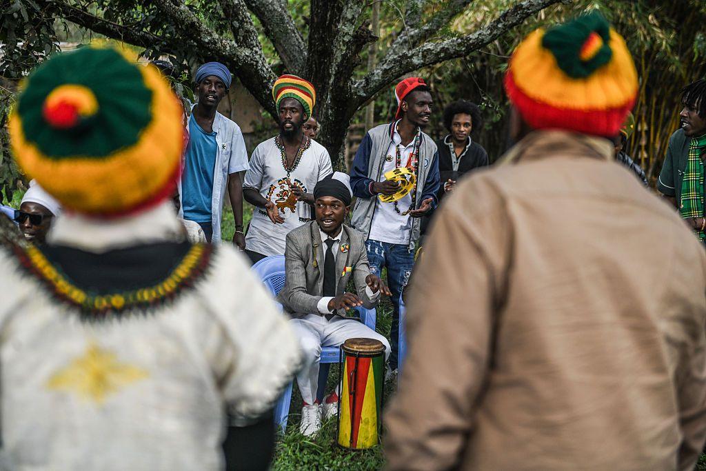 A group of Rastafarian people - some in stripped yellow, red and green hats - gather under a tree in Rongai, Kenya. One is playing a drum, another holds a tambourine as they sing and clap - Sunday 2 November 2025.