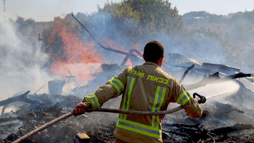 An Israeli firefighter puts out flames in a field after rockets launched from southern Lebanon landed on the outskirts of Kiryat Shmona, on June 4, 2024 