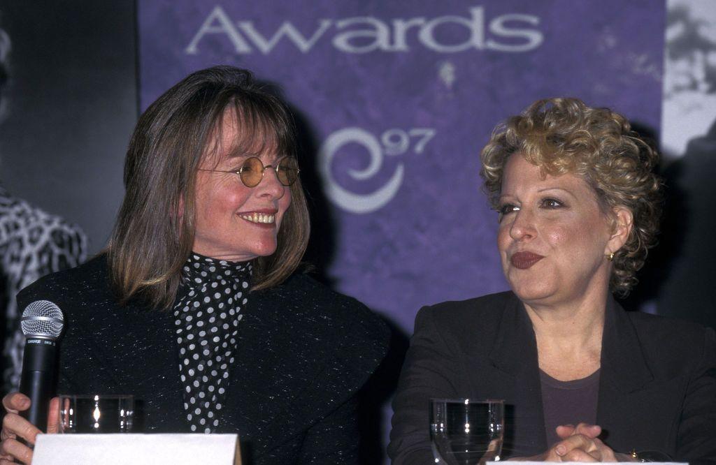 Diane Keaton looking and smiling at Bette Midler, both sitting at a table
