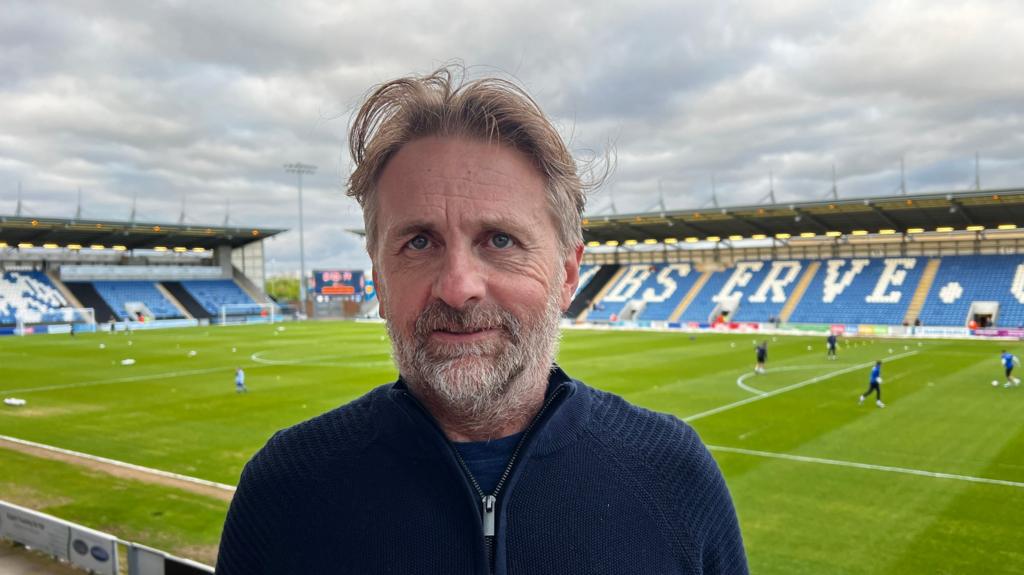 Robbie Cowling stood in front of Colchester United's pitch