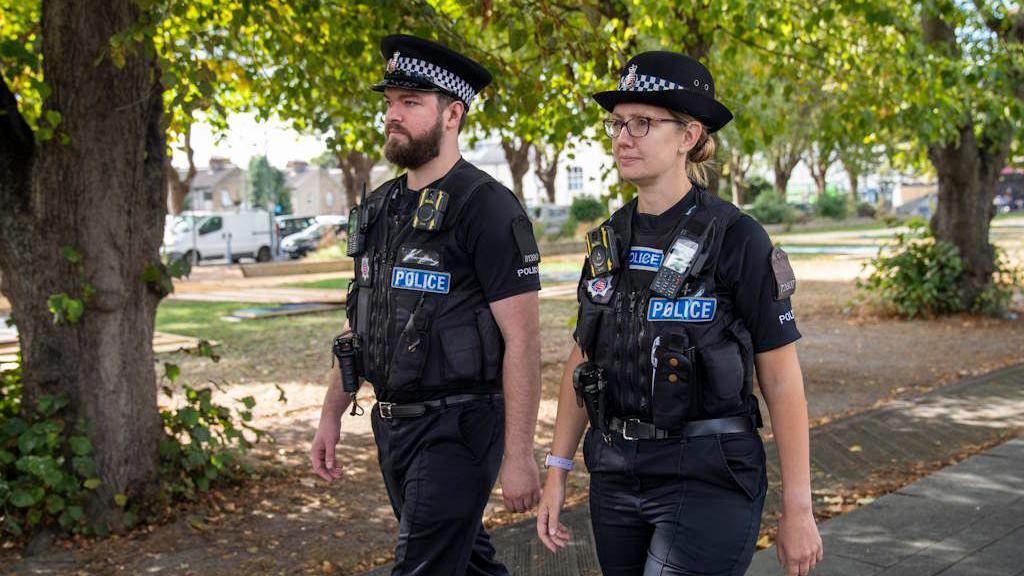 Two uniformed police officers walking through a green area in Southend-on-Sea