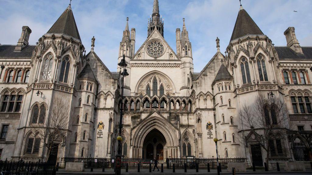 An exterior view of the Royal Courts of Justice in London. It shows a white, grand building with arched windows and doors.