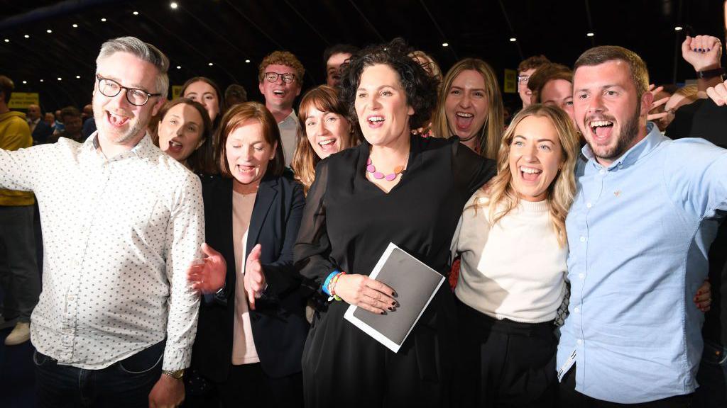 Claire hanna in black with supporters at election count centre Titanic