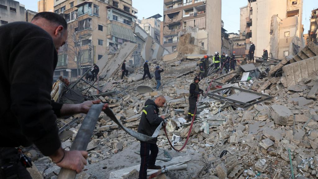 Men feed a fire hose over rubble in the debris after a strike in Beirut