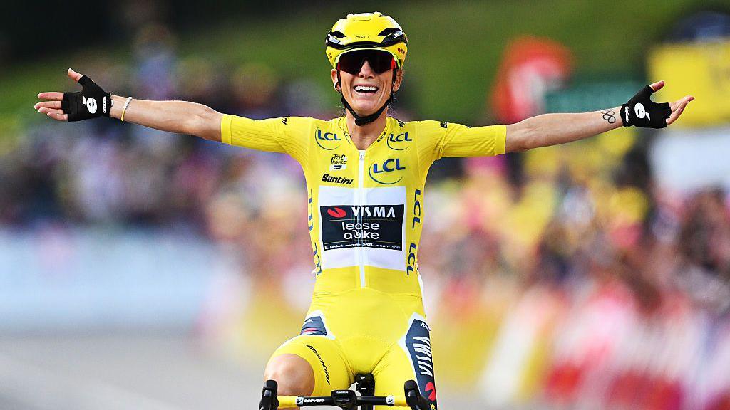 Pauline Ferrand-Prévot cycles with a huge smile, sitting up on the bike with her arms outstretched aftering winning the 2025 Tour de France Femmes last year. 