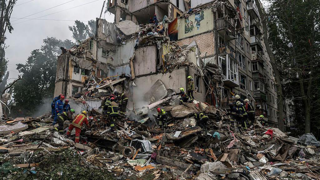 Firefighters and rescuers sift through the rubble of a destroyed building