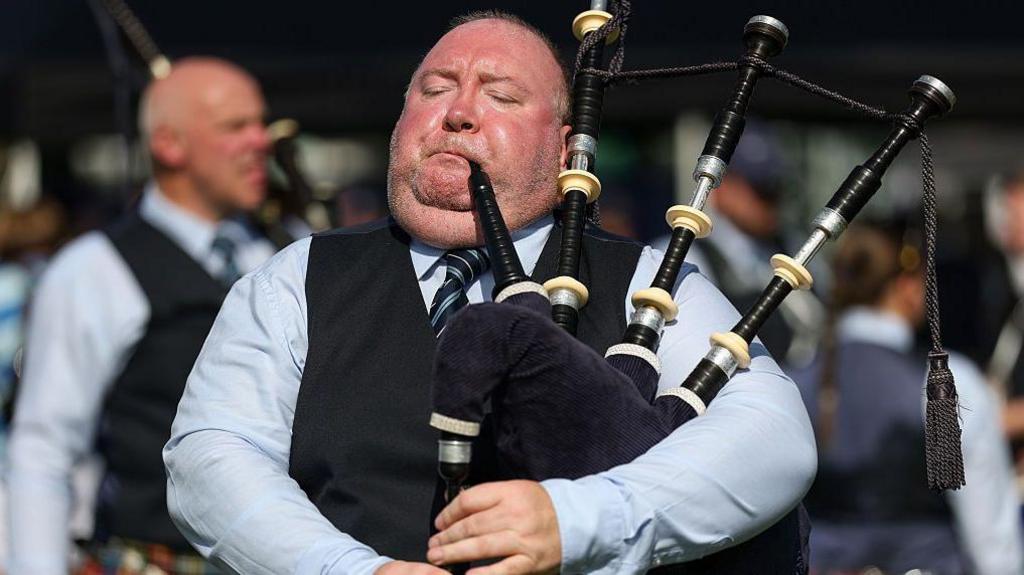 A piper with a red face puffs his cheeks out as he plays