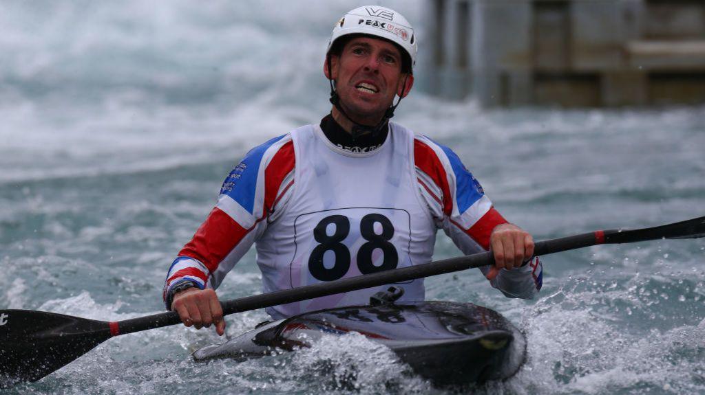 Etienne Stott competing in a canoe on water and holding an canoe paddle