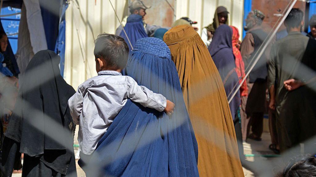 Afghan refugees - including two women wearing blue and yellow headscarfs - carrying a baby, arrive at a registration centre in Kandahar Province