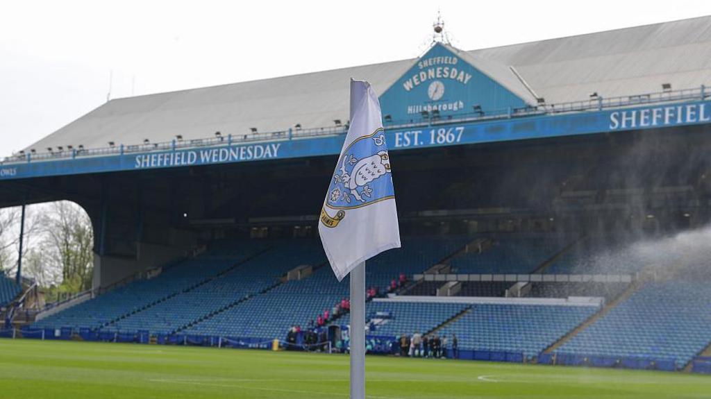 A corner flag bearing the Sheffield Wednesday badge sits in front of the south stand at Hillsborough