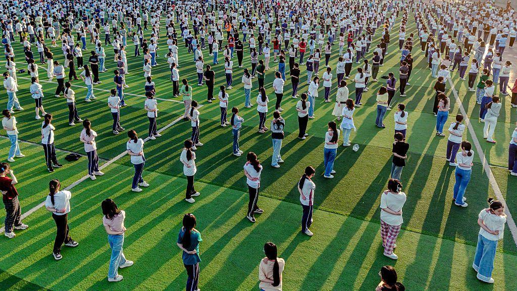 Hundreds of students practise yoga on a sports pitch to relieve stress before the annual China's National College Entrance Exam. They are spaced equally apart and are wearing normal clothes, not school uniform.