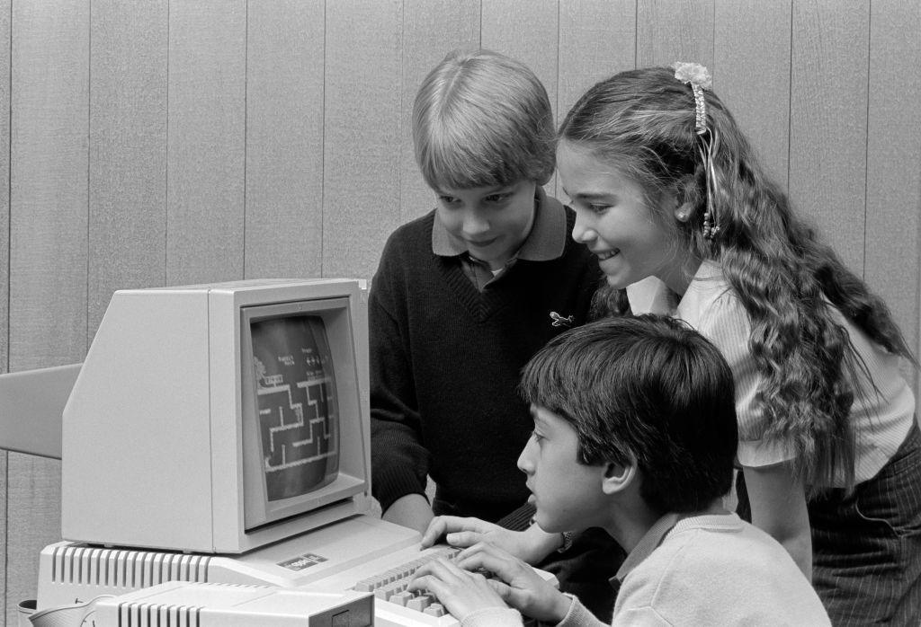 Black and white image of three children looking at a game on an old computer