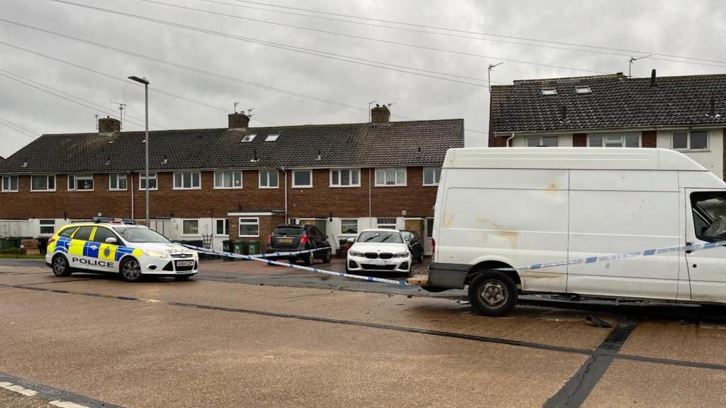 Wilton Avenue, Eastbourne, East Sussex. A police car is parked in the street, a white BMW and a white van (both damaged) are within a police cordon in the street.