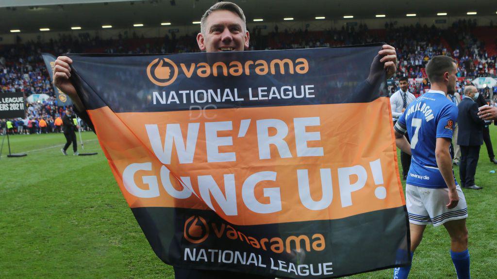 Dave Challinor holds up a "We are going up" banner celebrating Hartlepool's promotion in 2021