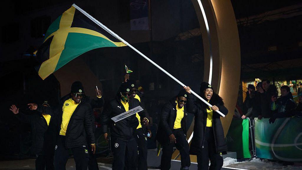 Former sprinter Mica Moore carries the Jamaican flag and leads her bobsleigh team through the opening ceremony in Milan-Cortina.