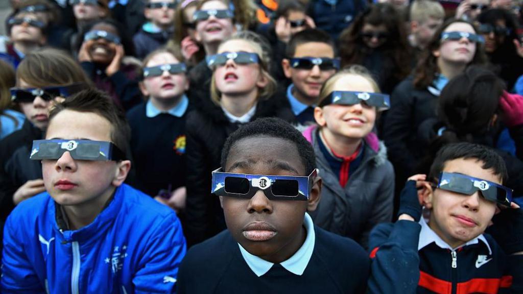A group of children watching an eclipse wearing special protective glasses.