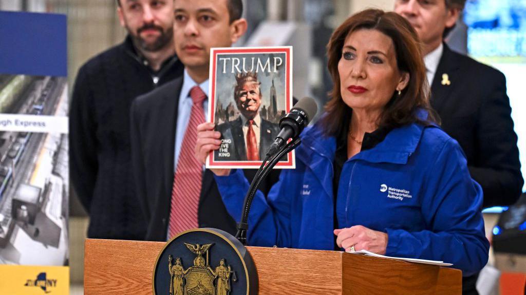 New York Governor Kathy Hochul holds up a photo of a fake magazine cover showing Donald Trump wearing a king's crown with the words, "long live the king" during a news conference in a subway station. 