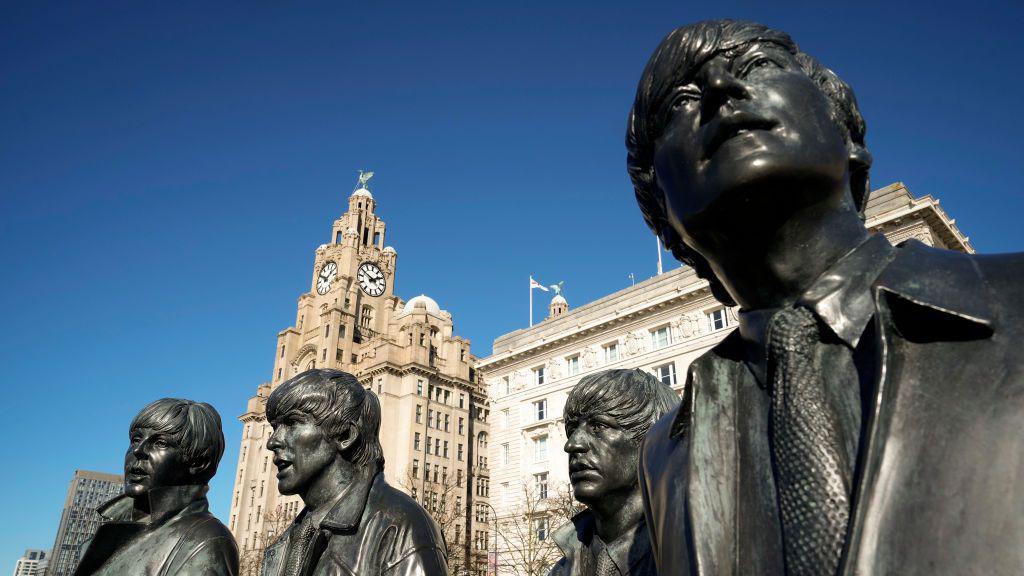 Cerfluniau efydd o’r Beatles yn Lerpwl, gyda’r Royal Liver Building yn y cefndir dan awyr las glir. 