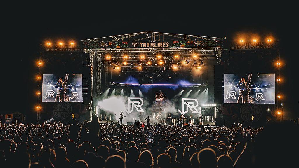 A crowd surrounds a stage where a band, The Reytons, play on stage at night.
